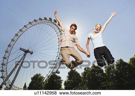 Young couple in park jumping in air in front of London Eye portrait low angle view View Large Photo Image Stock Photo - Young couple in park jumping in air in front of London Eye portrait low angle view. Fotosearch