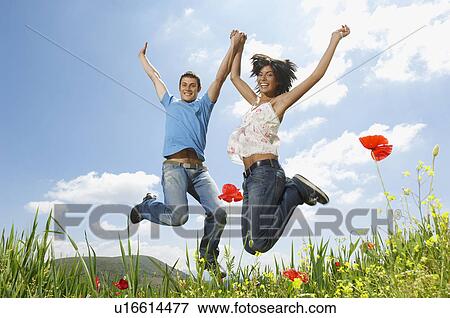 Stock Photo - Young couple jumping for joy in mountain meadow portrait low angle view. Fotosearch
