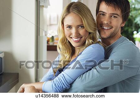 Stock Photo - Young couple looking at camera man holding woman. Fotosearch