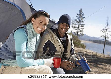 Young Couple sitting at campsite drinking from thermos View Large Photo Image Stock Photo - Young Couple sitting at campsite drinking from thermos. Fotosearch