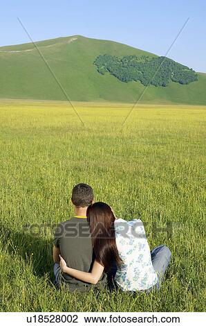 Young couple sitting in mountain field back view View Large Photo Image Stock Image - Young couple sitting in mountain field back view. Fotosearch