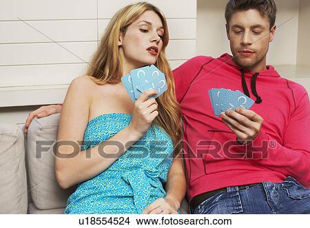 Picture - Young Couple sitting on sofa playing cards woman looking at cards of man. Fotosearch