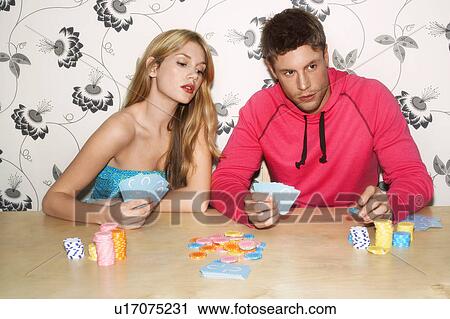 Stock Image - Young Couple sitting on sofa playing cards woman looking at cards of man. Fotosearch