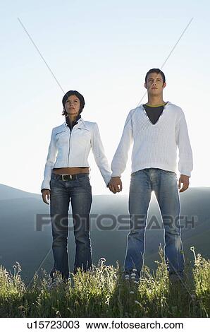 Young couple standing in mountain field looking at view front view low angle view View Large Photo Image Stock Image - Young couple standing in mountain field looking at view front view low angle view. Fotosearch