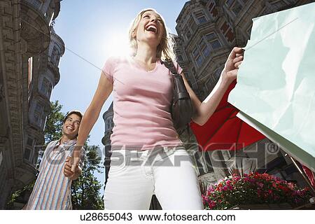Stock Image - Young couple walking down sity street holding shopping low angle view. Fotosearch