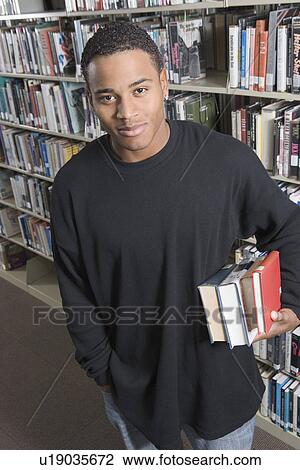 Young man holding books underarm in Library View Large Photo Image Stock Image - Young man holding books underarm in Library. Fotosearch
