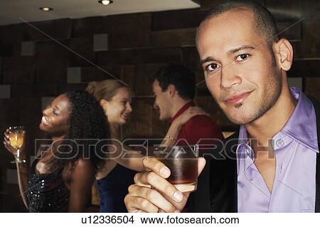 Picture - Young man holding drink standing in bar portrait. Fotosearch