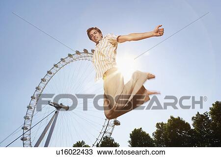 Young man in park jumping in front of London Eye portrait low angle view View Large Photo Image Stock Image - Young man in park jumping in front of London Eye portrait low angle view. Fotosearch