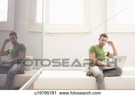 Stock Image - Young man with laptop on sofa. Fotosearch