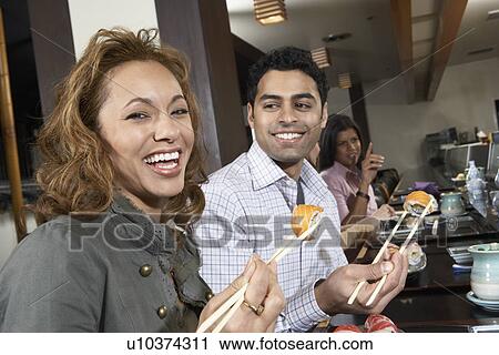 Young people eating sushi with chopsticks in restaurant View Large Photo Image Stock Image - Young people eating sushi with chopsticks in restaurant. Fotosearch