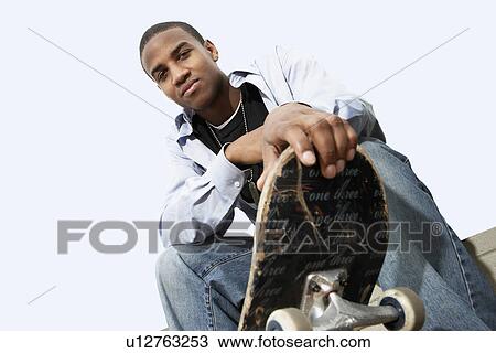 Stock Image - Young skateboarder sitting outside low angle view portrait. Fotosearch