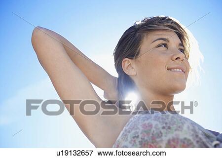 Young woman against blue sky holding hair close-up View Large Photo Image Stock Photo - Young woman against blue sky holding hair close-up. Fotosearch