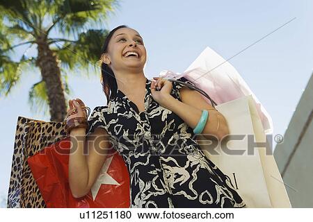 Stock Image - Young woman carrying shopping bags outdoors. Fotosearch