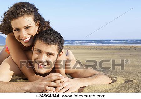 Picture - Young woman lying on back of man on beach portrait ground view. Fotosearch