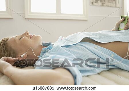 Stock Photography - Young woman lying on bed listening to music profile. Fotosearch