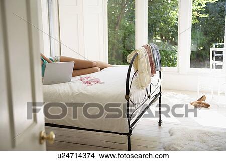 Young woman lying on bed using laptop low section View Large Photo Image Picture - Young woman lying on bed using laptop low section. Fotosearch