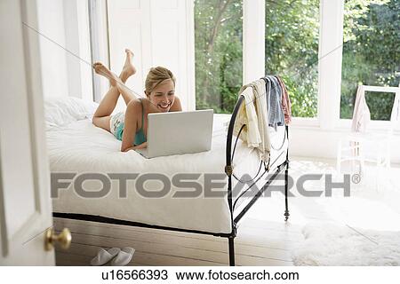 Young Woman lying on bed using laptop View Large Photo Image Stock Image - Young Woman lying on bed using laptop. Fotosearch