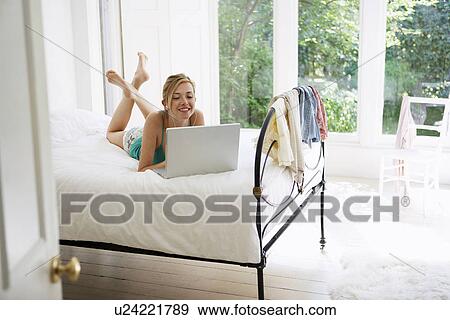 Young Woman lying on bed using laptop View Large Photo Image Stock Photo - Young Woman lying on bed using laptop. Fotosearch