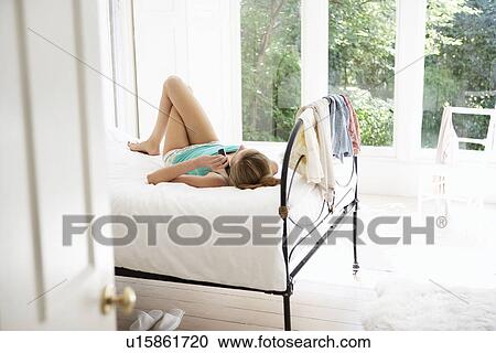 Young woman lying on bed using mobile phone View Large Photo Image Stock Image - Young woman lying on bed using mobile phone. Fotosearch