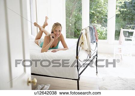 Young woman lying on bed using mobile phone portrait View Large Photo Image Stock Photo - Young woman lying on bed using mobile phone portrait. Fotosearch
