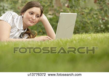 Young woman lying on grass using laptop. View Large Photo Image Stock Image - Young woman lying on grass using laptop.. Fotosearch