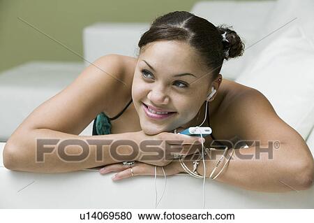 Young woman lying on sofa listening to MP3 player close up front view View Large Photo Image Stock Image - Young woman lying on sofa listening to MP3 player close up front view. Fotosearch
