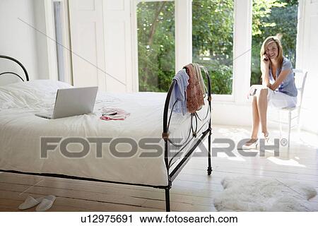 Young woman sitting in bedroom talking on cell phone portrait View Large Photo Image Stock Image - Young woman sitting in bedroom talking on cell phone portrait. Fotosearch