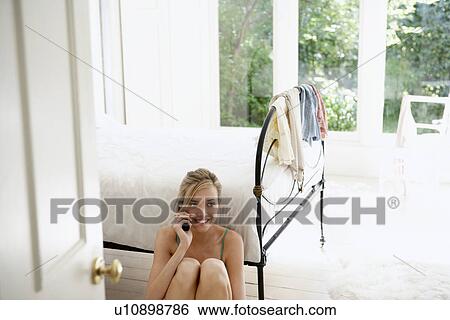 Young woman sitting on floor by bed on mobile phone View Large Photo Image Stock Photograph - Young woman sitting on floor by bed on mobile phone. Fotosearch