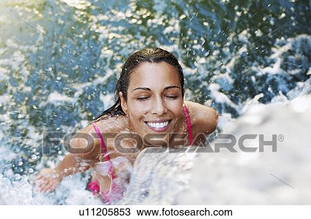 Stock Image - Young woman standing under waterfall high angle view. Fotosearch