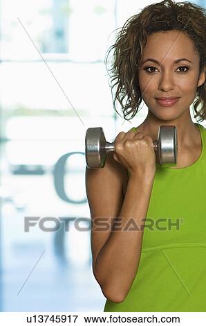 Stock Photo - Young woman using dumbbell indoors (portrait). Fotosearch