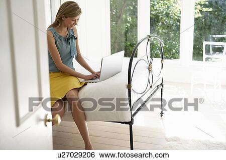 Stock Photograph - Young Woman Using Laptop on Bed. Fotosearch