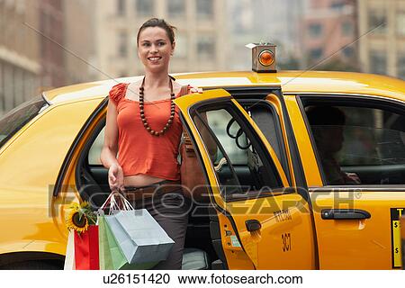 Stock Image - Young woman with shopping bags exiting yellow taxi cab. Fotosearch