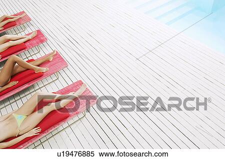 Stock Photography - Young Women Sunbathing by pool on deckchairs low section high angle view. Fotosearch