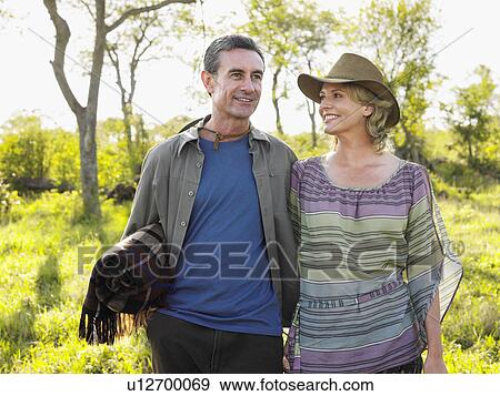 Stock Photo - Adult couple outdoors man carrying blanket woman wearing hat smiling. Fotosearch