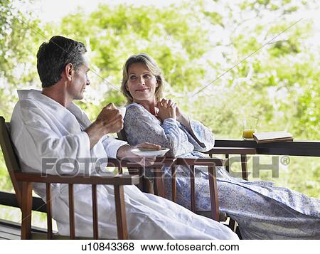 Stock Photo - Adult couple sitting on terrace man holding cup smiling. Fotosearch