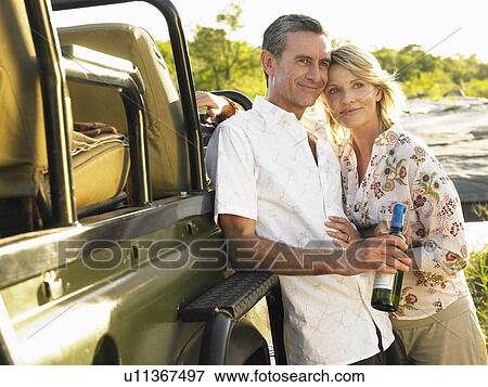 Adult couple standing by jeep man holding bottle of wine smiling View Large Photo Image Stock Photo - Adult couple standing by jeep man holding bottle of wine smiling. Fotosearch