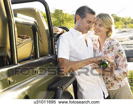 Stock Photography - Adult couple standing by jeep man pouring wine smiling. Fotosearch