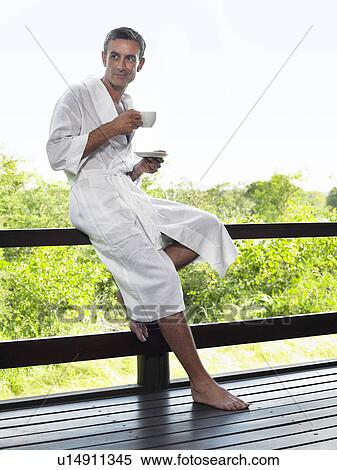 Adult man in bathrobe leaning on terrace railing holding cup View Large Photo Image Stock Photography - Adult man in bathrobe leaning on terrace railing holding cup. Fotosearch