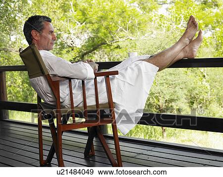 Stock Photo - Adult man in bathrobe sitting on chair at terrace with feet up. Fotosearch