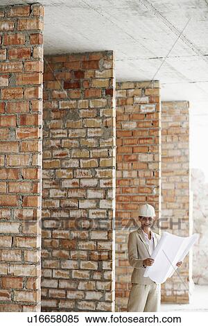 Stock Photography - Architect holding plans at construction site. Fotosearch