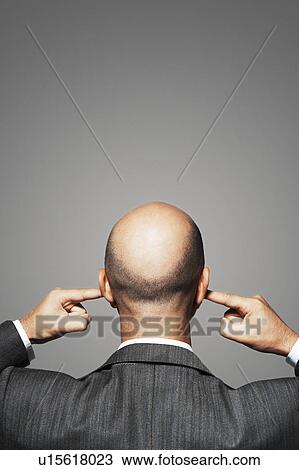 Stock Image - Balding businessman with fingers in ears back view. Fotosearch