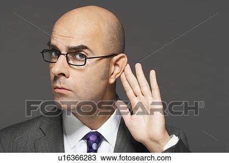 Stock Image - Balding man with hand behind ear listening closely. Fotosearch
