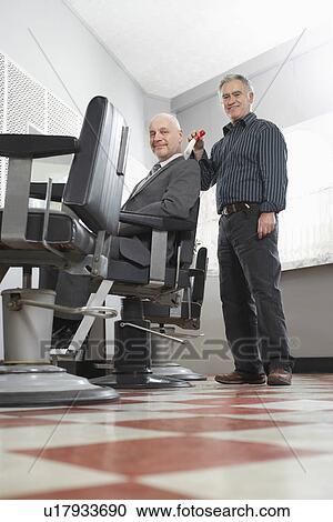 Stock Image - Barber brushing business mans head in barber shop portrait. Fotosearch