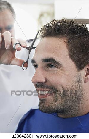 Stock Image - Barber cutting mans hair in barber shop close-up. Fotosearch