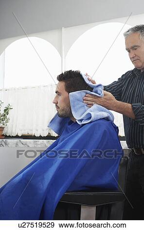 Stock Photo - Barber preparing man for haircut in barber shop. Fotosearch