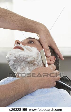Stock Photograph - Barber shaving man in barber shop close-up. Fotosearch