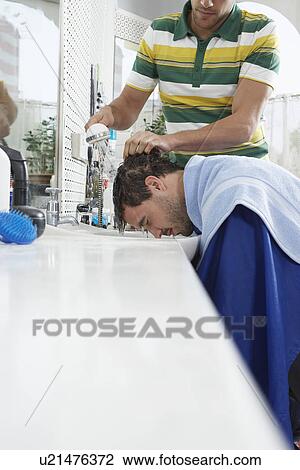 Stock Image - Barber washing mans head in barber shop. Fotosearch