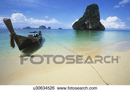 Stock Photograph - Boat on beach lone rock formation in background. Fotosearch