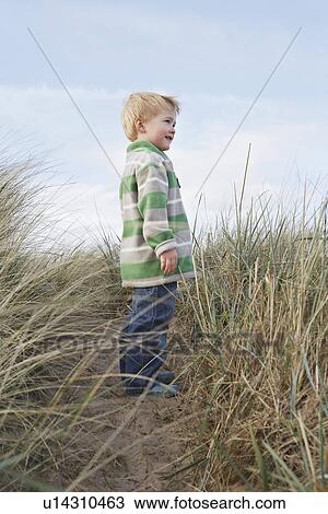 Stock Image - Boy (3-4) standing on path among long grass. Fotosearch
