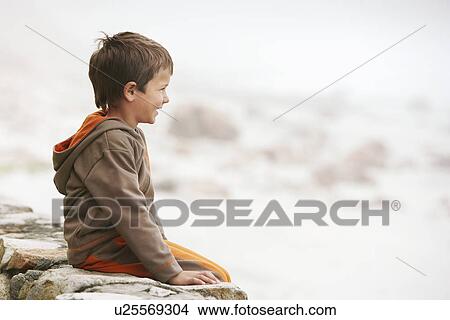 Boy (5-6) sitting on wall on beach View Large Photo Image Picture - Boy (5-6) sitting on wall on beach. Fotosearch